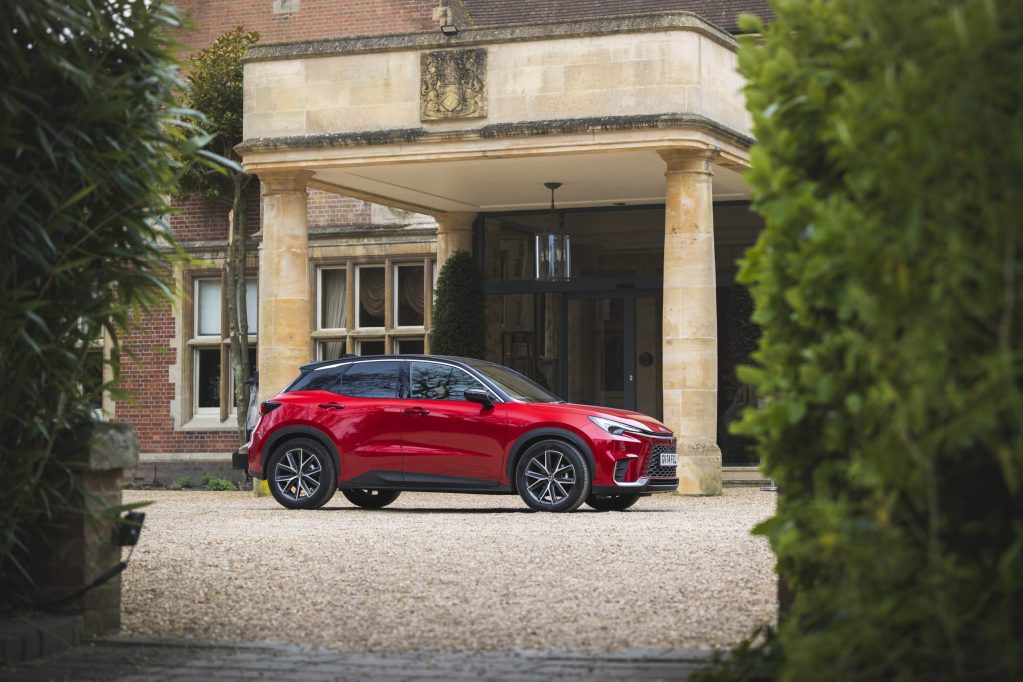 A red Lexus LBX parked in front of a grand entrance to a building, surrounded by greenery.