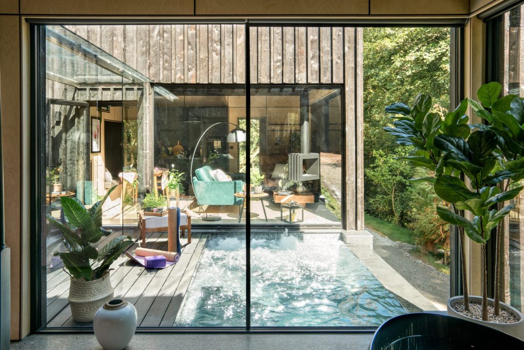 Interior view of a modern spa cabin with a small pool and lush greenery visible through large glass windows.