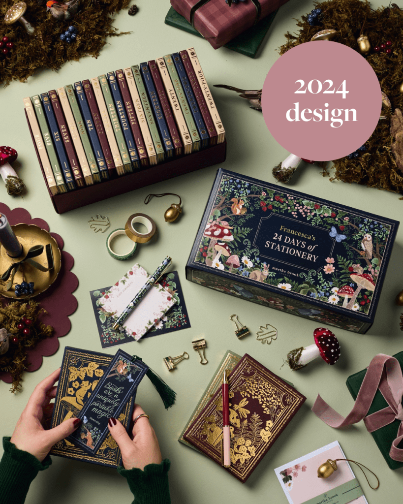 A hands-on image of a beautifully designed stationery advent calendar for 2024, featuring intricate patterns and vibrant colors, alongside various stationery items including pens, paper clips, and decorative cards, set on a green background.