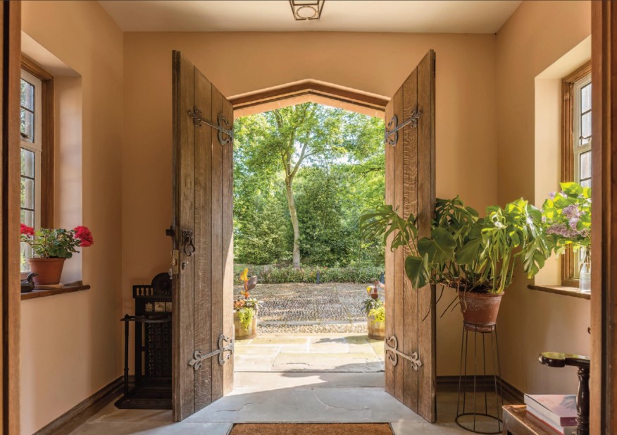A view from the entrance of a Georgian house, featuring wooden double doors open to a garden with greenery. Potted plants are placed on either side of the doorway, creating a welcoming atmosphere.