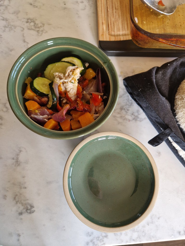 A green stoneware bowl filled with chopped vegetables and chicken, placed next to a smaller empty bowl on a marble countertop.