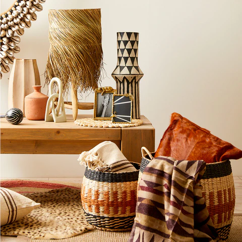 A cozy interior scene showcasing a wooden table adorned with decorative items, including woven baskets, a textured lamp, geometric vases, and hand-crafted textiles, all reflecting South African design elements.