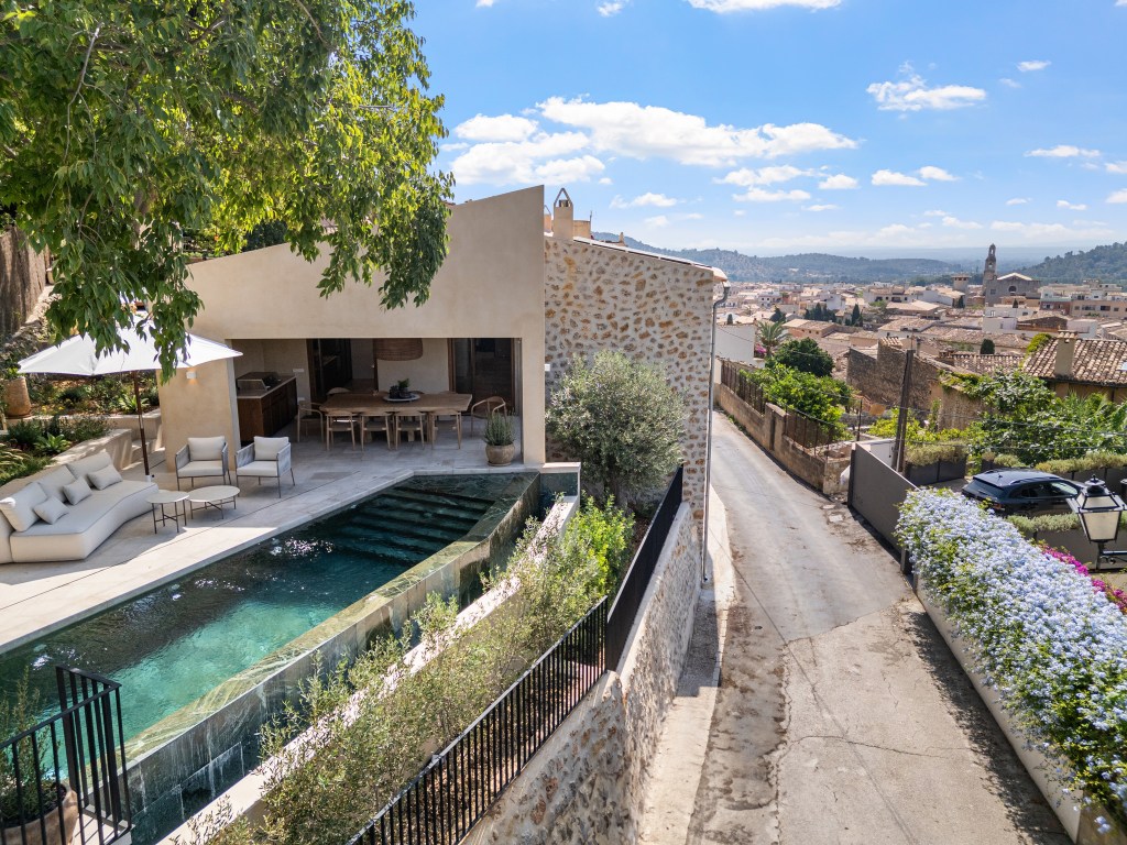 Aerial view of a contemporary house in Alaró, featuring a salt-water infinity pool, outdoor seating area, and panoramic views of the village and mountains.