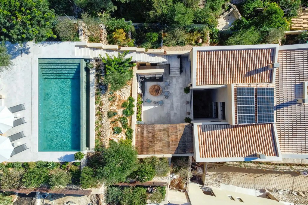 Aerial view of a modern residential property in Mallorca featuring a swimming pool, landscaped gardens, solar panels, and spacious outdoor seating areas.