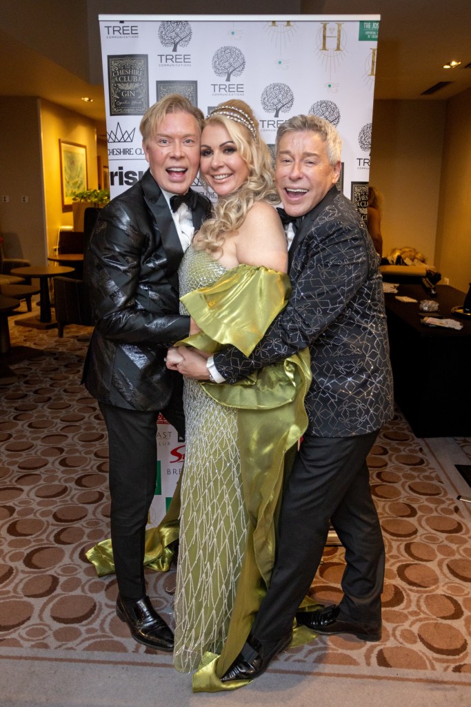 Three attendees at the Crème de la Crème Cheshire Business Awards 2025 posing together, dressed in glamorous attire, with a branded backdrop featuring logos for The Joshua Tree and The Cheshire Club.