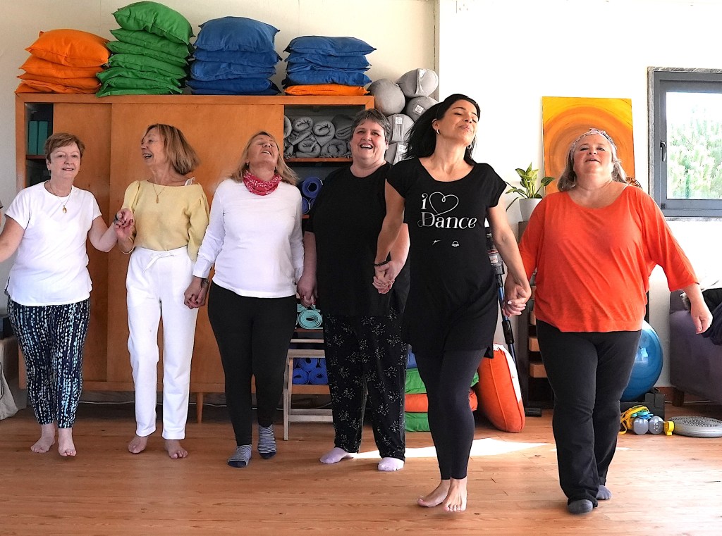 Six women holding hands and dancing in a wellness retreat setting, showcasing a joyful and supportive atmosphere.